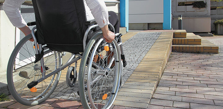 Rollstuhlfahrer an Rollstuhlrampe vor Wohnhaus