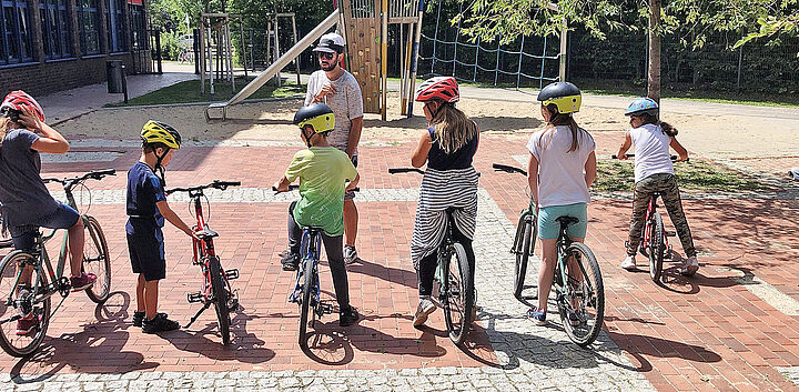 Mehrer Kinder in einer Reihe sitzen auf einem Fahrrad
