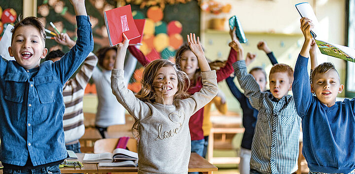 Kinder in Schulklasse reißen die Hände hoch