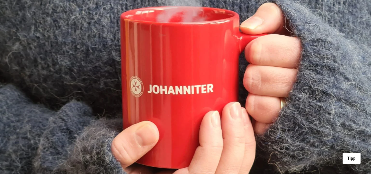 Rote Tasse von zwei Händen gehalten mit der Aufschrift Johanniter